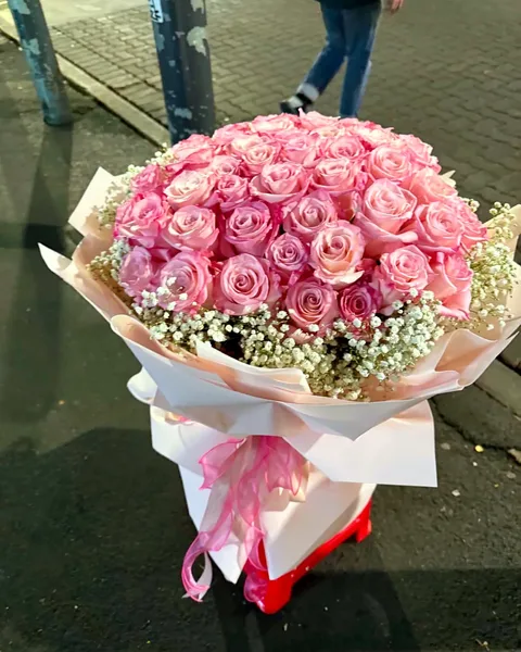 A huge round bouquet of pink roses on a red stool in the laneway at night
