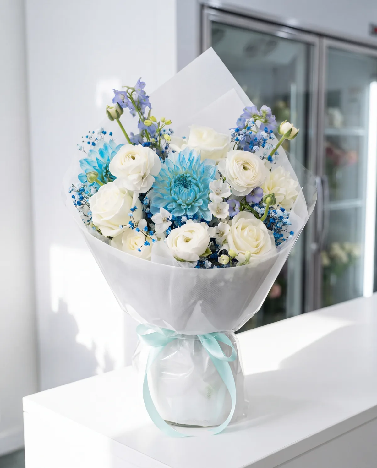 Their white ranunculus, roses and blue dahlia bouquet with a mint ribbon, on a white bench